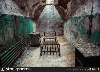 Abandoned prison cell room with old rusty bed frame and peeling walls