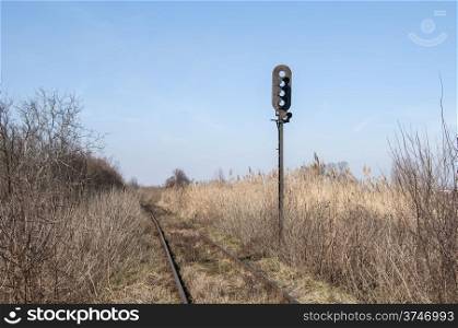 Abandoned rail line and empty railway traffic light in dry grass field