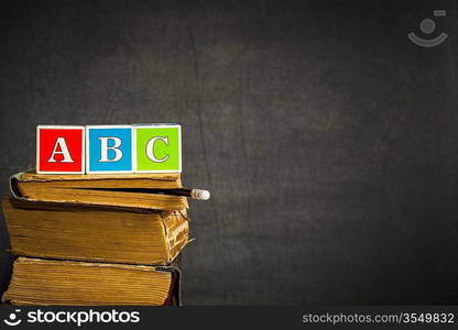 ABC on old books against blackboard with space for text. School concept