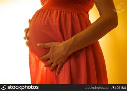 Abdomen of pregnant women in pink dress on the backlight