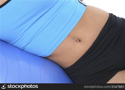 Abdomen with belly button ring in blue and black workout clothes. Laying against blue exercise ball.