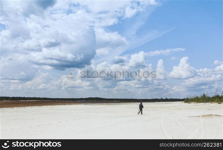 Aboriginal man in the distance walking across a sandy desert with sparse plants under a beautiful blue sky with huge cumulus clouds. Conceptual wide summer landscape. Selective focus.