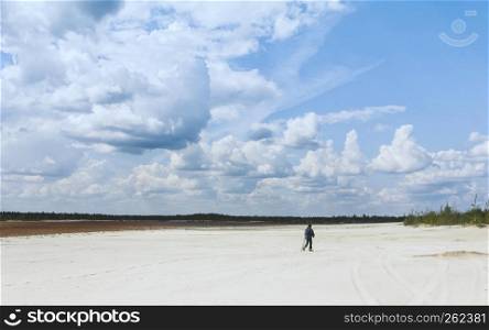 Aboriginal man in the distance walking across a sandy desert with sparse plants under a beautiful blue sky with huge cumulus clouds. Conceptual wide summer landscape. Selective focus.