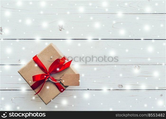 Above brown Gift box and red Ribbon, Snow with tag on white wood background with space.