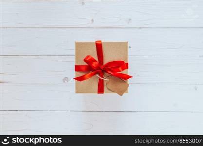 Above brown gift box with tag on wooden board background. Gift box with red ribbon on wooden white background with space.