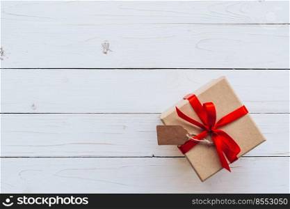 Above brown gift box with tag on wooden board background. Gift box with red ribbon on wooden white background with space.