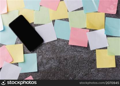 Above many blank paper stick note list with the modern black smart mobile phone blank screen on concrete background, Business smartphone reminder concept