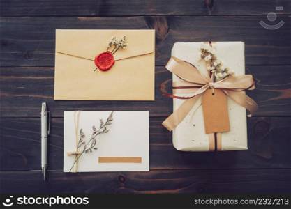 Above of craft gift box and greeting card with pen on wood table background