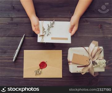 Above of hand girl hold card and craft gift box on wooden table background