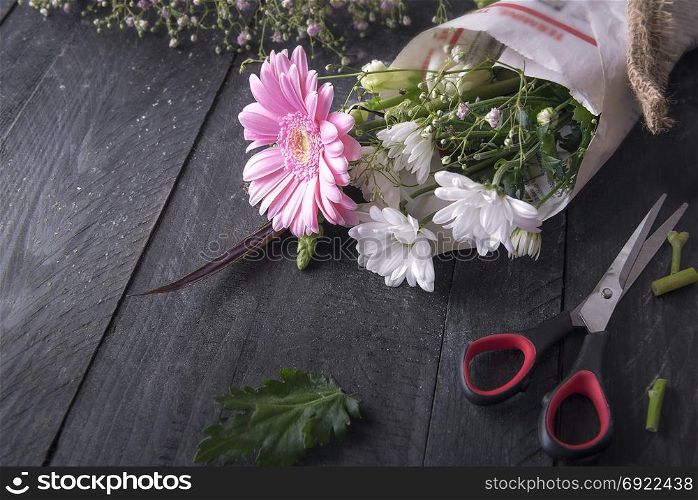Above view image about the activity of flower packaging, with a bouquet of chrysanthemum flowers wrapped in newspaper, surrounded by scissors and leftovers from plants.