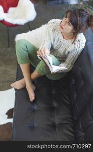 Above view of a beautiful young smiling woman sitting on leather couch relaxing while holding a book at home. Isabella Antonelli