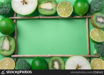 Above view of a frame made from fresh green fruits and broccoli, on a green table. Healthy eating frame. Detox context. Diet food. Vegetarian aliments.