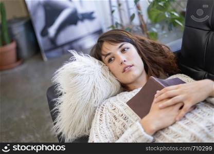 Above view of beautiful young smiling woman lying on leather couch relaxing while holding a book at home. Rafa Fernandez
