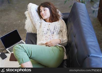 Above view of beautiful young smiling woman lying on leather couch relaxing while holding a book at home. Rafa Fernandez