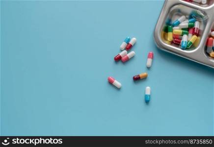 Above view of Colorful antibiotic capsule pills on a tray and blue background. Antibiotic drug resistance. Antimicrobial drugs. Prescription drugs. Pharmaceutical industry. Health care and medicine.