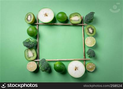 Above view of green fruits and vegetables displayed on a square frame from bamboo sticks, on a green background. Vegetarian food. Detox context.
