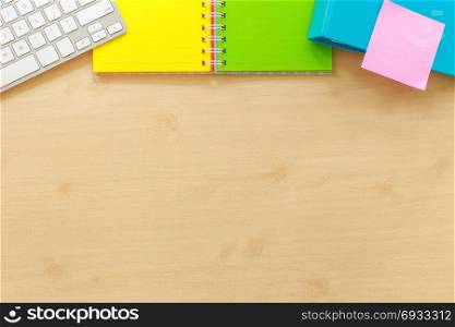 Above view of office workplace with blank desk space. Colorful paper book, keyboard, folder and pink sticky note on top side. Documents and time management concepts, mockup background flame.
