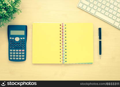 Above view of open book with yellow blank pages, calculator, keyboard, plants and black pen on office table background. Resolution goals and planning concepts. Sepia tone, vintage and retro styles.
