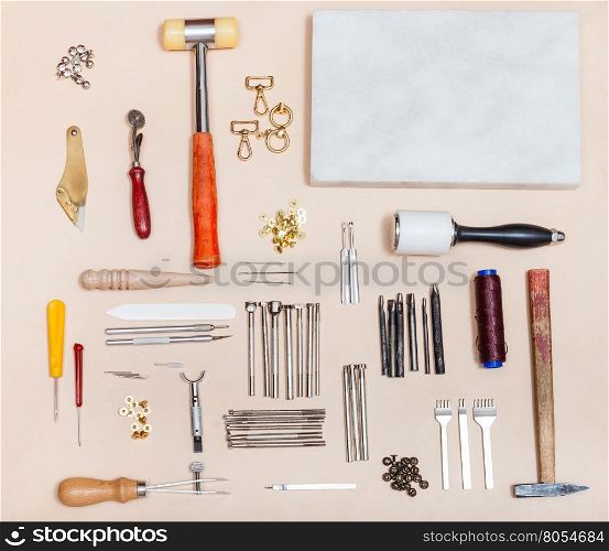 above view of set of various leathercraft instruments and marble board on natural leather surface