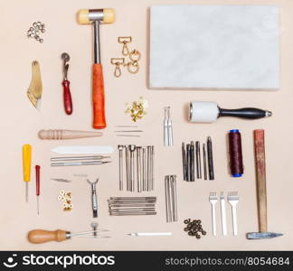 above view of set of various leathercraft instruments and marble board on natural leather surface