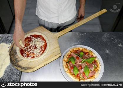 Above view on chef hand adding cheese to pizza base with sauce. Man pizzaiolo working on professional kitchen. Above view on chef hand preparing pizza base on professional kitchen