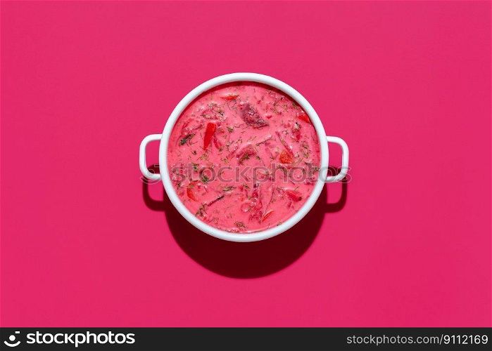 Above view with a bowl of borscht, ukrainian beetroot soup, on a magenta background. Enamel bowl with beetroot soup and sour cream.