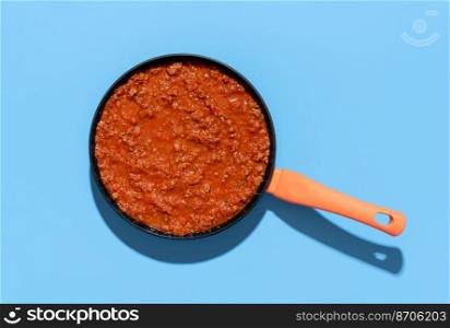 Above view with a pan with bolognese sauce isolated on a blue background. Classic italian sauce with minced meat and tomato sauce