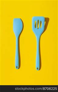 Above view with a set of blue kitchen utensils minimalist on a yellow table. Set of 2 blue spatulas isolated on a yellow-colored background