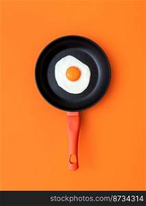 Above view with a sunny side up egg in an iron cast pan on a orange colored table. Cooking pan with a single fried egg on a colorful background.
