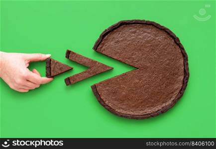 Above view with a woman’s hand taking a tiny slice of chocolate tart, minimalist on a green background.