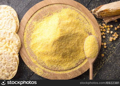 Above view with corn flour on a round wooden platter surrounded by corn cakes, corn cob and grains, on a vintage table.