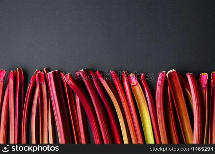 Above view with rhubarb stalks aligned on a black background. Fresh vegetables. Organic rhubarb stems on a black table