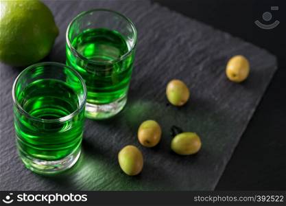 Absinthe with lime and green olives on a dark background. Absinthe with lime and green olives