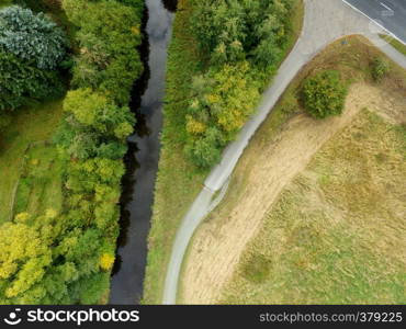 Abstract aerial view of a straightened stream next to a meadow with a large, isolated green tree, made by drone