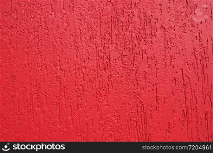 Abstract background and texture of a plastered wall in bright red with bark beetle texture. Illuminated by the bright sun.