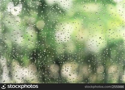Abstract background from raindrop on glasses window with blurred green tree background. Fresh nature concept.