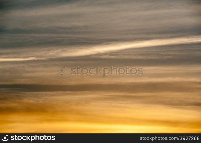 Abstract background of sky and clouds in horizontal streaks at sunset, glowing orange at bottom and dark at top.