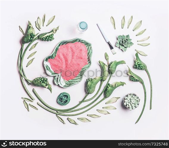 Abstract beauty composing with green tropical leaves and flowers and bowl with sea salt on white table background, top view, flat lay. Natural skin care, spa and cosmetic concept