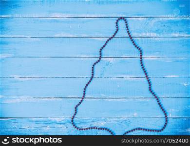 abstract blue wooden background with outline of a Christmas tree of red garlands, empty space on the left