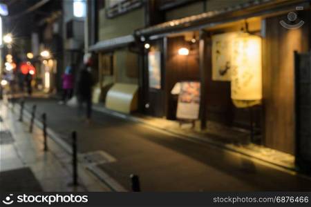 Abstract blur people walking on narrow street of wooden store and restaurant with lighted lantern at night in Kyoto, Japan