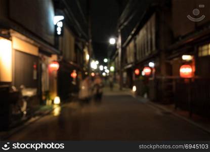 Abstract blur people walking on narrow street of wooden store and restaurant with lighted lanterns at night in Kyoto, Japan
