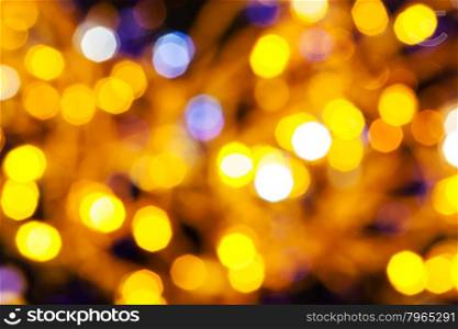 abstract blurred background - dark yellow and violet twinkling Christmas lights bokeh of electric garlands on Xmas tree