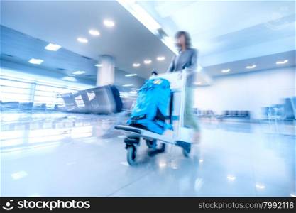 Abstract blurred image of traveling woman in airport terminal pushing luggage cart. Art toning. Travel concept background