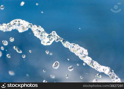 Abstract close-up of illuminated water stream falling into focus against blurred blue background.