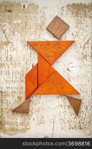 abstract figure of a female dancer built from seven tangram wooden pieces, a traditional Chinese puzzle game; rough white painted barn wood background