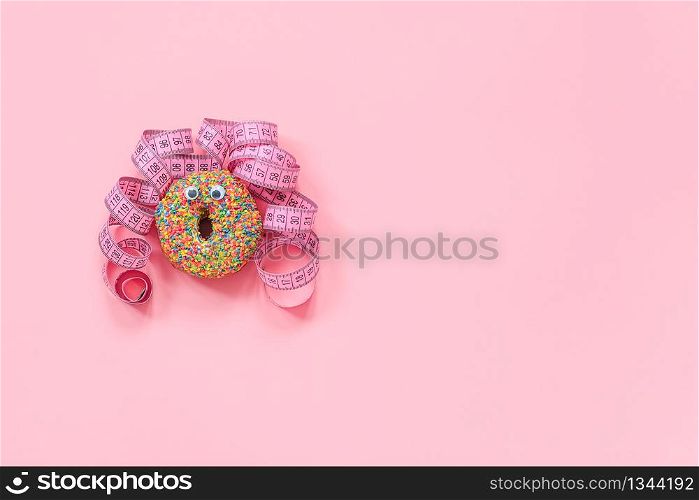 Abstract funny face of woman from donut with eyes and hair from centimeter tape on pink background. Diet or unhealthy food concept Top view Flat lay Copy space.. Abstract funny face of woman from donut with eyes and hair from centimeter tape on pink background. Diet or unhealthy food concept Top view Flat lay Copy space