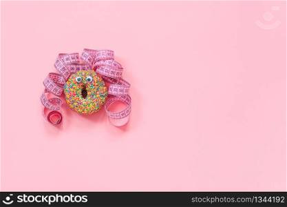 Abstract funny face of woman from donut with eyes and hair from centimeter tape on pink background. Diet or unhealthy food concept Top view Flat lay Copy space.. Abstract funny face of woman from donut with eyes and hair from centimeter tape on pink background. Diet or unhealthy food concept Top view Flat lay Copy space