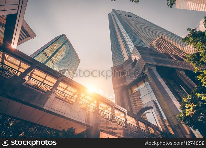 Abstract futuristic cityscape view with modern skyscrapers. Sun shines in the sunset sky, reflecting in glass of the footbridge. Urban architecture background. Hong Kong