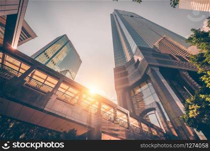 Abstract futuristic cityscape view with modern skyscrapers. Sun shines in the sunset sky, reflecting in glass of the footbridge. Urban architecture background. Hong Kong