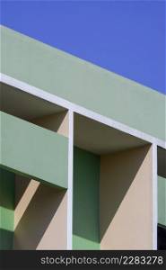 Abstract geometric pattern background of shading fin concrete on modern green and beige building wall against blue clear sky in vertical frame